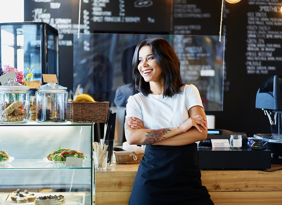 Business Insurance - Portrait of a Smiling Young Female Business Owner Standing in Front of the Counter at her Cafe While Looking Outside
